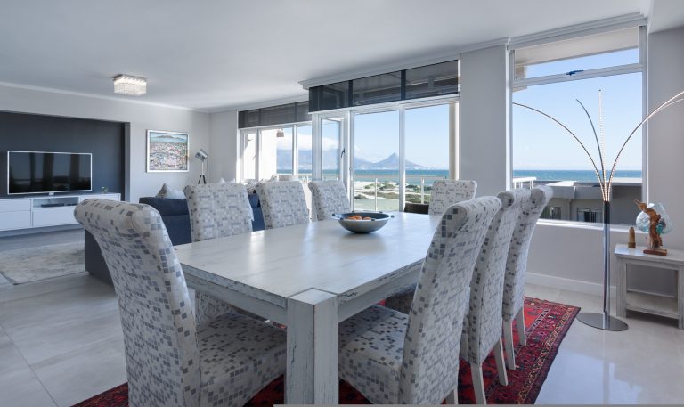 Moderno ambiente open space che integra zona living e sala da pranzo, caratterizzato da un tavolo da pranzo con sedie in tessuto e una vista panoramica sul mare