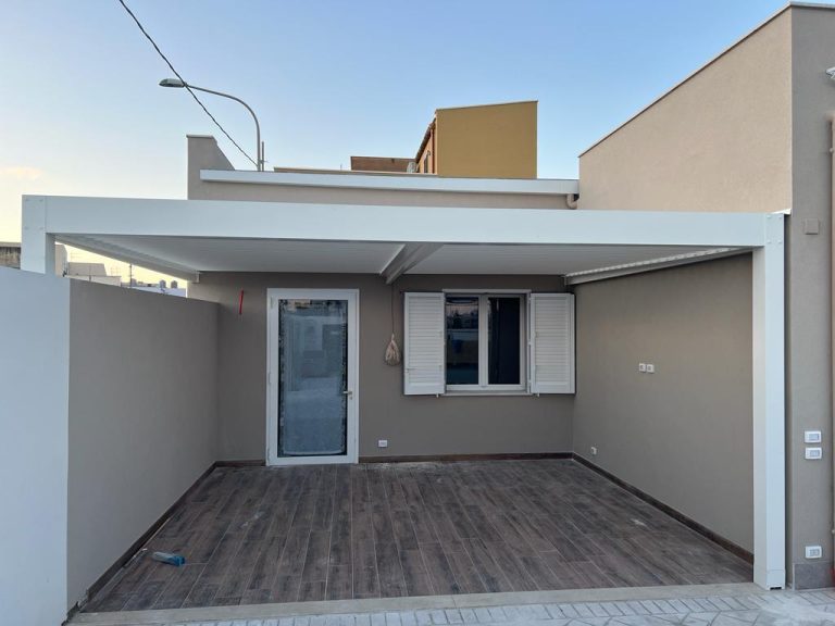 Moderna pergola addossata in alluminio bianco, utilizzata come copertura per un patio esterno