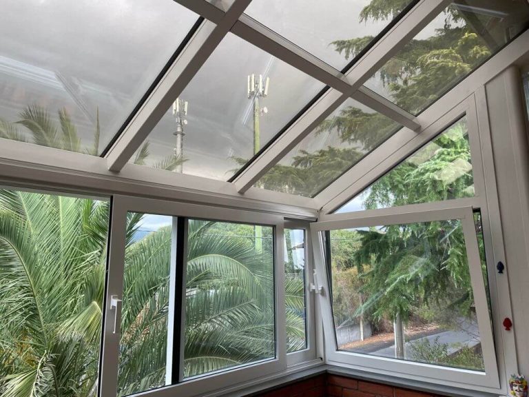 Veranda chiusa con infissi in PVC bianco e ampie vetrate, adibita a zona relax con vista sugli alberi